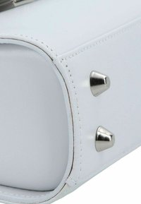 Coin de sac à main en simili cuir blanc avec des accents de clous métalliques argentés et des détails de couture visibles. Texture lisse et forme structurée.