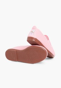 Zapatos de tela rosa tipo slip-on con suelas de goma, suelas en color terracota y una pequeña etiqueta con un diseño de mono en el talón.