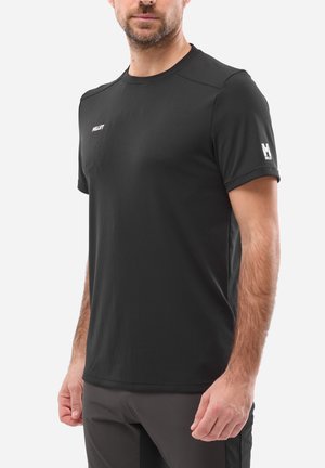 Homme portant un t-shirt de sport noir à manches courtes avec des logos "Millet" sur la poitrine et la manche gauche, assorti à un pantalon gris foncé.