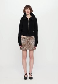 Svart zip-up tröja med hög krage, ihop med en minikjol i leopardtryck och svarta sandaler med remmar. Slät tyg och åtsittande design.