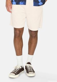 Light beige textured shorts with a relaxed fit, paired with brown canvas sneakers and white crew socks.