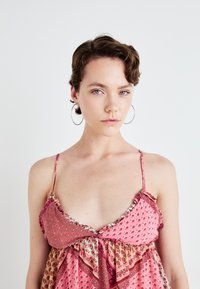 Abito rosa a fantasia con spalline sottili, caratterizzato da motivi floreali e dettagli arricciati. Il tessuto ha una leggerezza e una fluidità piacevole.