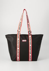 Bolsa tote de nylon negra con asas a rayas rojas y blancas que presenta el texto "HUNTER". Incluye un parche central con logo y un diseño espacioso.