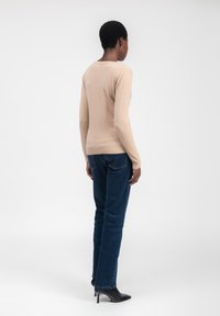 Beige körperbetonter Pullover mit langen Ärmeln, runder Ausschnitt und geripptem Saum, kombiniert mit dunkelblauen Jeans und schwarzen spitzen Pumps.