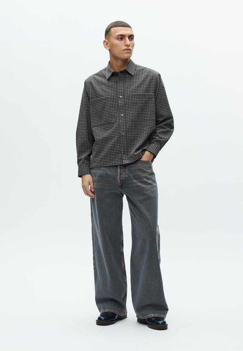 Checkered button-up shirt in black and gray, paired with loose-fitting dark denim jeans, featuring a straight leg and subtle fraying at hems.