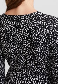 Mustavalkoinen kuvioitu mekko, jossa on pyöreä pääntie, haarautuva kangas abstraktilla pistekuvioinnilla ja muotoiltu vyötärö.