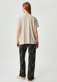 Lichtgrijs katoenen T-shirt gecombineerd met zwarte pyjamabroek met een wit sterrenpatroon. Zachte textuur met een relaxte pasvorm.
