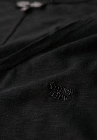 Zwarte katoenen T-shirt met een subtiele textuurafwerking en een geborduurd "Superdry" logo aan de onderzijde aan de linkerkant.