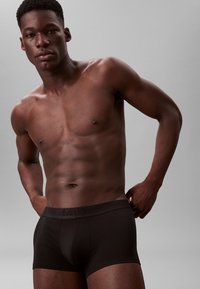 Czarne slipy Calvin Klein z logo, dopasowany krój, materiał bawełniany i gładka tekstura, noszone przez modela o umięśnionej budowie ciała.