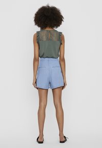 Green top with lace back and cap sleeves, paired with light blue high-waisted shorts. Textured fabric with pockets and a relaxed fit.