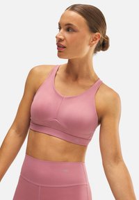 Sujetador deportivo rosa claro hecho de una tela suave, con tirantes anchos, un diseño sin costuras y un sutil detalle del logo cerca del dobladillo.
