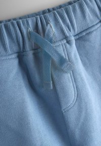 Nærbillede af lyseblå joggingbukser med ribbet elastisk linning med bundet flad snor og synlig søm på forlommerne.