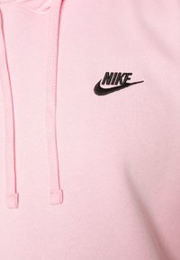 Rosa hoodie tillverkad av mjukt material, med en svart Nike-logotyp på bröstet, snörning och design av känguruficka.
