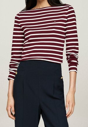 Haut à manches longues rayé bordeaux et blanc avec un col bateau, associé à un pantalon ajusté bleu marine avec un bouton accent doré.