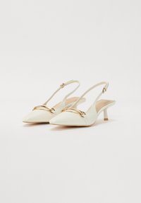 Valkoinen keinonahkainen slingback-kengät, joissa on terävä kärki, kultaketjuakseli vampin yli ja matala kitten-korko.