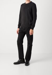 Felpa nera con collo rotondo, caratterizzata da un piccolo logo. Abbinata a jeans neri a gamba dritta e scarpe nere lucide.