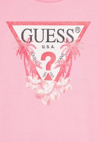 Roza bombažna majica s tremi koti featuring belo in rdeče trikotno logo s palmami, cvetličnimi motivi ter črnim besedilom "GUESS U.S.A." in "1201 1203."