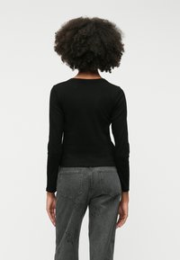 Čierny top s dlhými rukávmi vyrobený z elastického materiálu, priliehavý v páse. Kombinovaný s vysokými sivými džínsami s vyšitými vzormi.