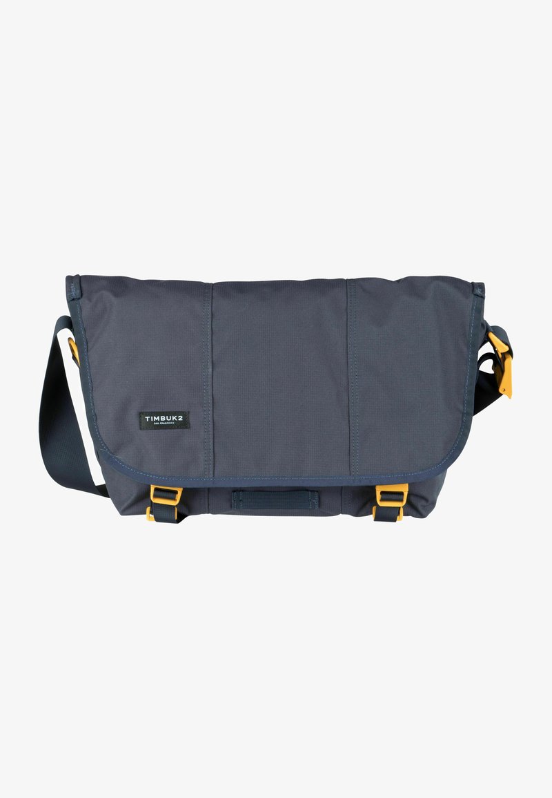Borsa a tracolla in tessuto grigio scuro con patta ripiegabile, accenti blu navy, accessori gialli e tracolla regolabile. Presenta una superficie testurizzata.