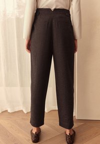 Dunkelgraue, maßgeschneiderte Hose mit geradem Schnitt, zwei Gesäßtaschen und Knopfakzenten, kombiniert mit Loafern im Leopardenmuster.