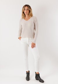 Maglione a maglia tessurizzata color beige chiaro con scollatura a V e maniche lunghe, abbinato a jeans bianchi slim fit e stivaletti neri alla caviglia.