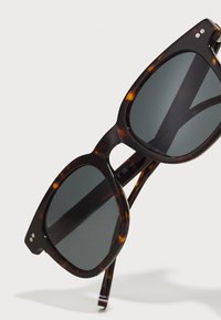 Lunettes de soleil carrées avec un motif écaille de tortue, verres gris foncé et monture brillante. Dotées d'accents en métal sur les côtés de la monture et de branches fines.