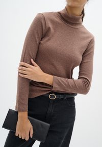 Bordázott, barna garbós hosszú ujjú felső, fekete magasderekú farmernadrággal és fekete clutch táskával, arany színű övcsattal.