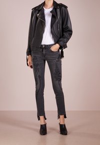 Persona vistiendo una chaqueta de cuero negra sobre una camisa blanca, jeans gris oscuro bordados con dobladillos deshilachados y botas de tobillo negras con tacón.