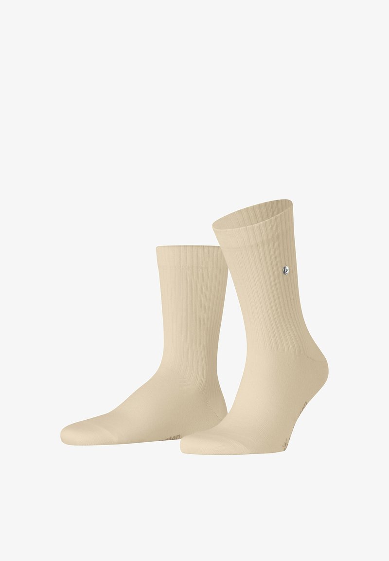 Paire de chaussettes beige côtelées à tige courte avec un petit logo rond argenté sur le côté extérieur d'une chaussette, sur fond blanc.