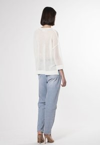 Übergroßer, weißer Strickpullover mit offenem Maschenmuster, Dreiviertelärmel, kombiniert mit hellblauen, hoch taillierten Jeans und nude-farbenen Absätzen.