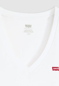Balta medvilninė marškinėliai su V formos iškirpte, kairėje krūtinės pusėje mažas raudonas Levi's logotipas ir viduje etikėtė su priežiūros instrukcijomis.