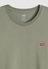 Olīvu zaļa kokvilnas T-kreklu ar ribotu apkakli un mazu sarkanu Levi's logo plāksteri kreisajā krūtī. Gluda tekstūra, standarta piegriezums.