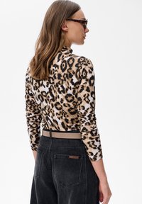 Top z długim rękawem w panterkę o dopasowanym kroju, w zestawieniu z czarnymi dżinsami z wysokim stanem i beżowym paskiem. Gładka faktura materiału.