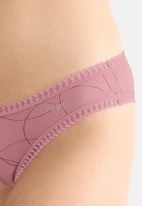 Roze kanten lingerie met een golvende rand, bestaande uit een gladde stof en subtiele cirkelpatronen. Elastische tailleband voor comfort.
