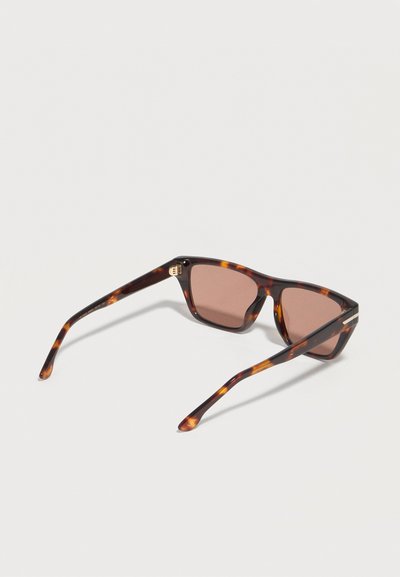 Καφέ αποχρωματισμένα ορθογώνια γυαλιά ηλίου με σκελετό από σχέδιο χελώνας και λεπτούς βραχίονες, εκτεθειμένα σε λευκή επιφάνεια.