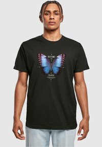 Black cotton t-shirt featuring a large blue butterfly graphic with purple accents and white text saying "BECOME THE CHANGE." Short sleeves.