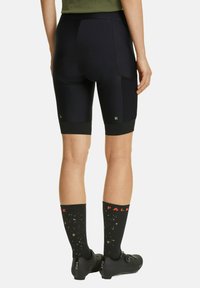 Pantaloni da ciclismo neri con imbottitura sul retro, pannelli in rete e accenti riflettenti verdi. Abbinati a calze nere al ginocchio con un motivo a macchie.