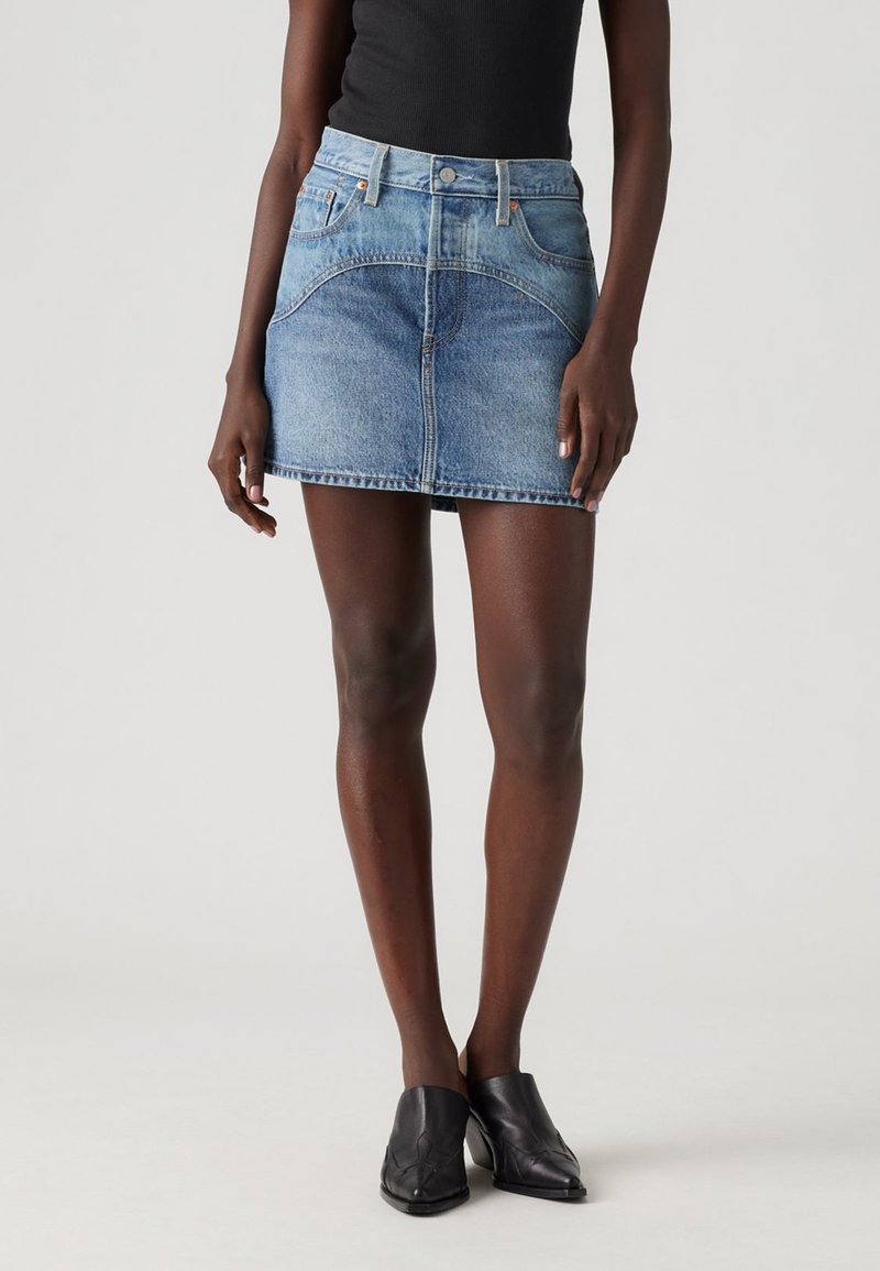 Denim mini svārki ar augstu jostasviju, gaiši zilā krāsā un pieguļošā dizainā. Iespējami priekšējie kabatas un priekšējais pogu aizdare.
