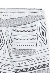 Tissu blanc avec des motifs tribaux géométriques noirs et une poche rectangulaire cousue.