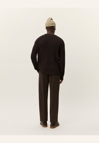 Dark brown knitted sweater with a round neckline, long sleeves, and ribbed hem, paired with tailored brown trousers and brown shoes.