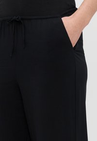 Svarte vide bukser med snor i livet, med sidelommer og en glatt, myk tekstur. Enkelt design, uten mønstre eller detaljer.
