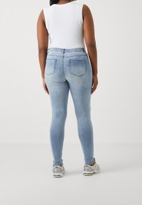 Ljusblå skinny jeans i denim, med medelhög midja, bakfickor och en mjuk textur, kombinerade med grå träningsskor.