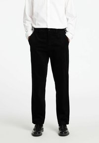 Črne kord volna hlače s ravnim krojem, z elastiko v pasu, sprednjimi žepi in subtilno vertikalno teksturo. Usklajene z črnimi čevlji.