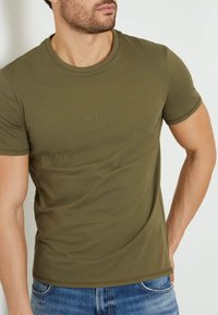 Olivengrøn bomulds T-shirt med rund halsudskæring og korte ærmer; har et diskret prægede logo på brystet.