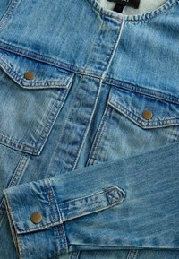Lichtblauwe denim jack met twee borstzakken, metalen knopen en contrasterende stiksels. Heeft een ronde kraag en lange mouwen.