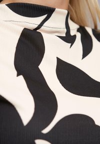 Tessuto a righe in bianco e nero caratterizzato da grandi motivi di foglie astratte. Design con collo alto e una cucitura pulita. Aspetto texturizzato.