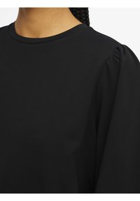 Schwarzes Oberteil mit rundem Halsausschnitt und gepufften kurzen Ärmeln, aus einem glatten, matten Stoff gefertigt. Einfaches Design ohne sichtbare Muster.