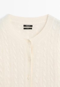 Cardigan en laine couleur crème avec motif torsadé, col rond et trois boutons assortis à l'avant.