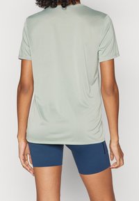 Camisa atlética de manga corta verde claro con una textura suave, con un cuello redondo y un corte relajado. Combinada con pantalones cortos de ciclismo azules.