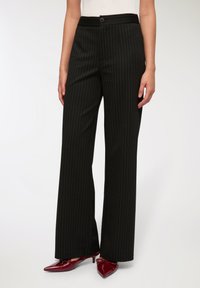 Czarne spodnie w cienkie paski o luźnym kroju, z zapięciem na guzik w talii i gładką fakturą. Połączone z błyszczącymi burgundowymi butami.